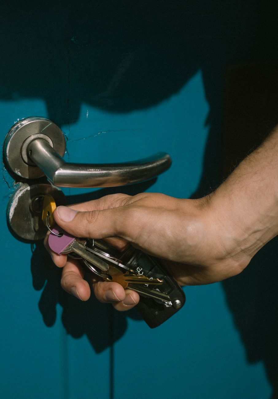 Una mano introduce la llave en la cerradura de una puerta azul con manilla metálica.