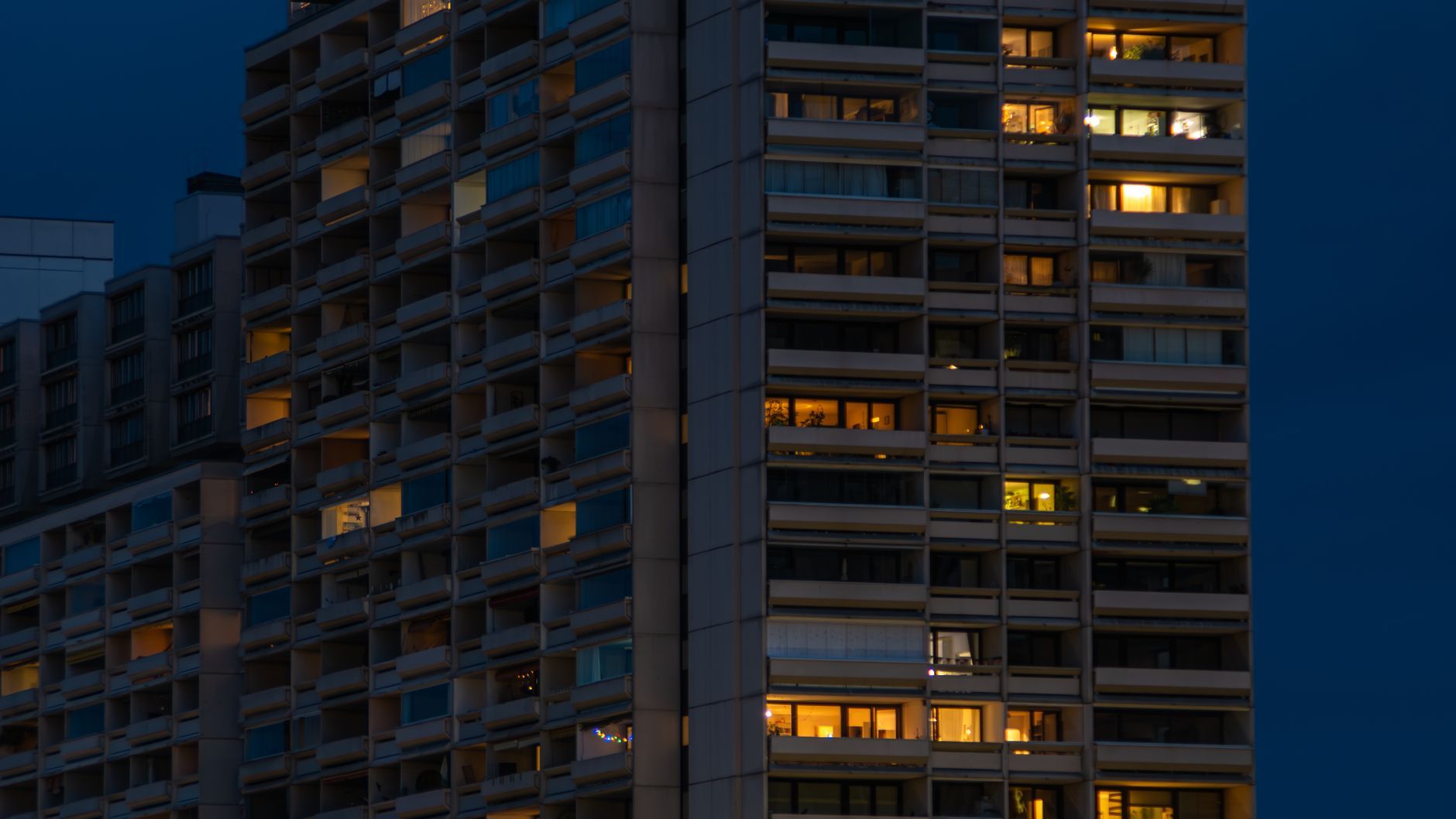 Torre de viviendas iluminada al anochecer, con las ventanas encendidas.
